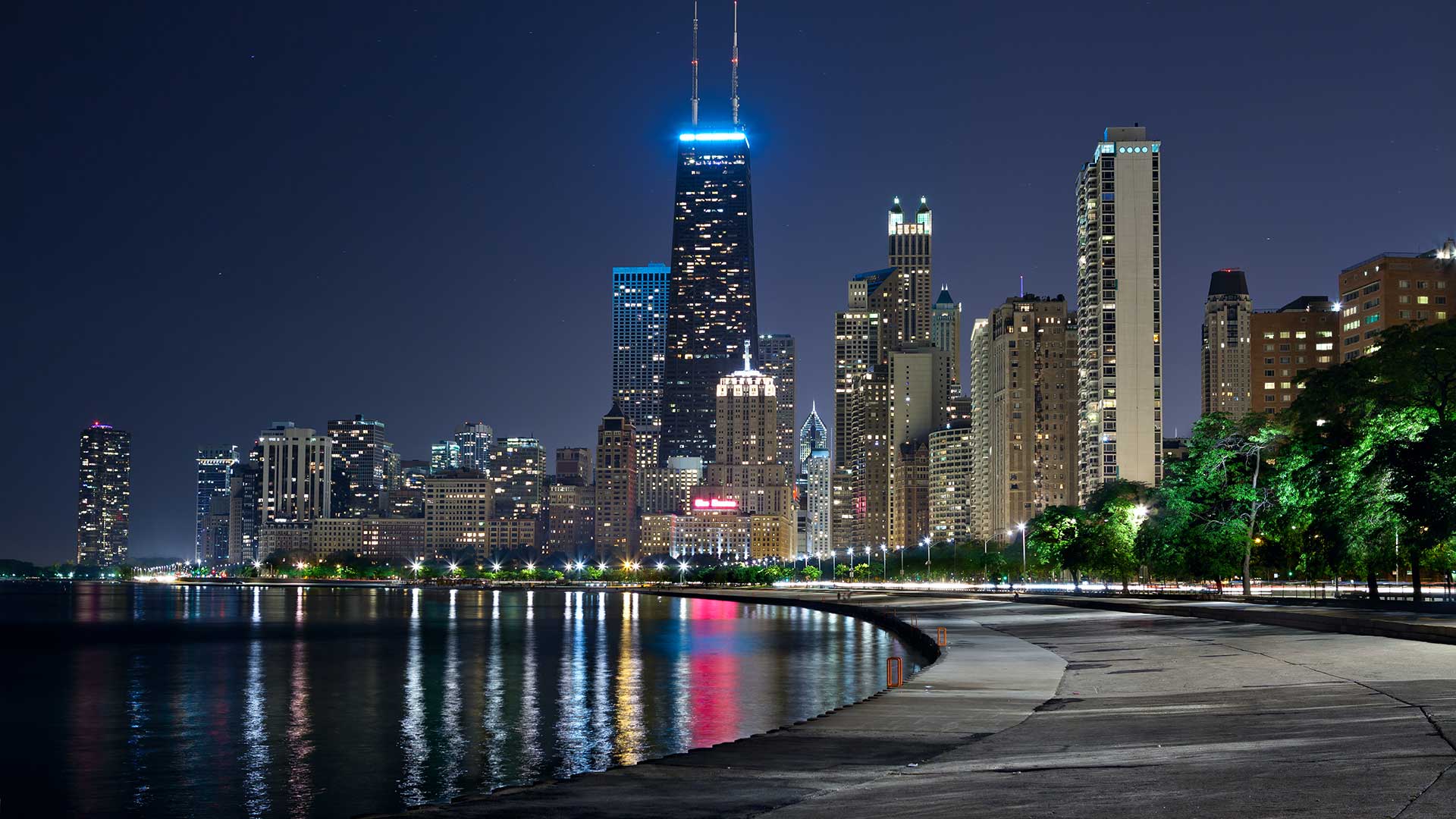 Looking south towards downtown Chicago from along Lake Shore Drive and the Gold Coast at night. The skyline is lit up with many colorful lights.