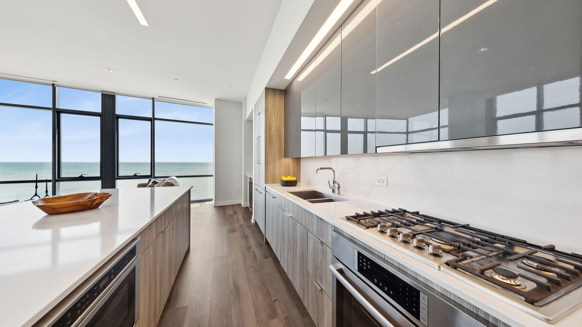 A modern kitchen with stainless steel appliances, an island, and a view of the ocean through large windows.